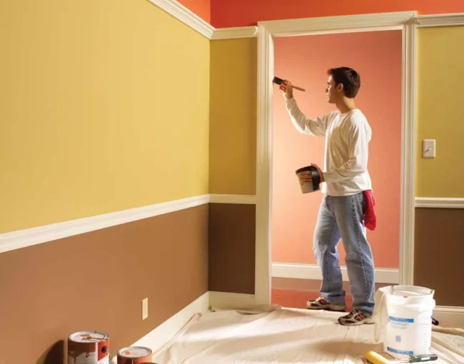 Professional painter meticulously painting a room with yellow and brown walls. AZ Painting Ltd.